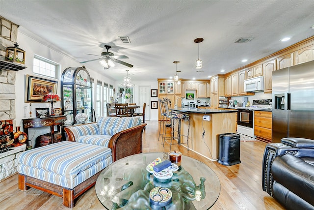 living room with visible vents, light wood-style flooring, and ceiling fan with notable chandelier