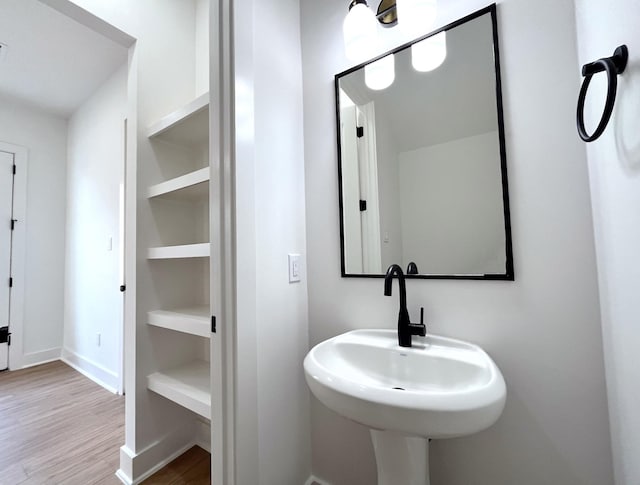 bathroom featuring baseboards, a sink, built in shelves, and wood finished floors