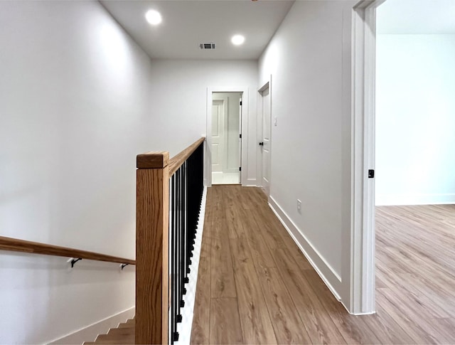 hallway featuring baseboards, wood finished floors, visible vents, and an upstairs landing