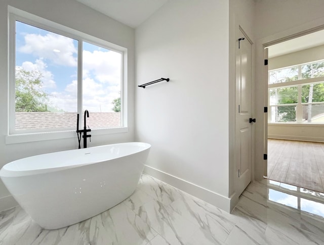 full bath with baseboards, marble finish floor, and a freestanding bath