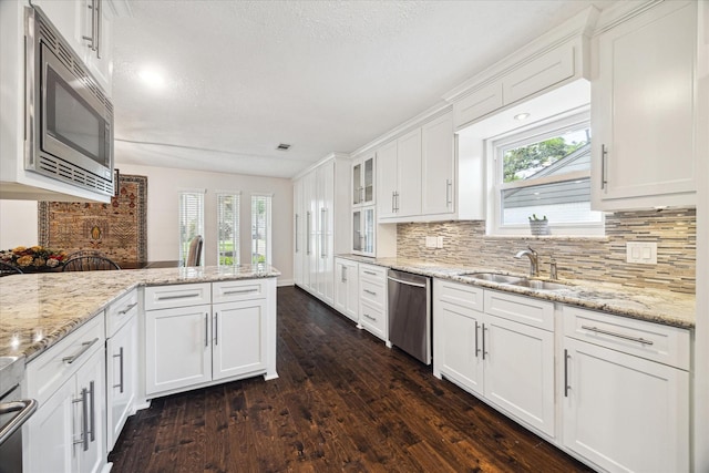 kitchen with tasteful backsplash, a sink, dark wood-style floors, stainless steel appliances, and white cabinetry