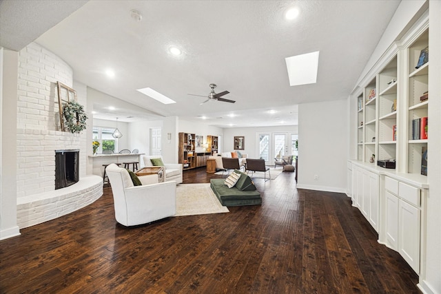 living area featuring dark wood-type flooring, a ceiling fan, a brick fireplace, and a skylight