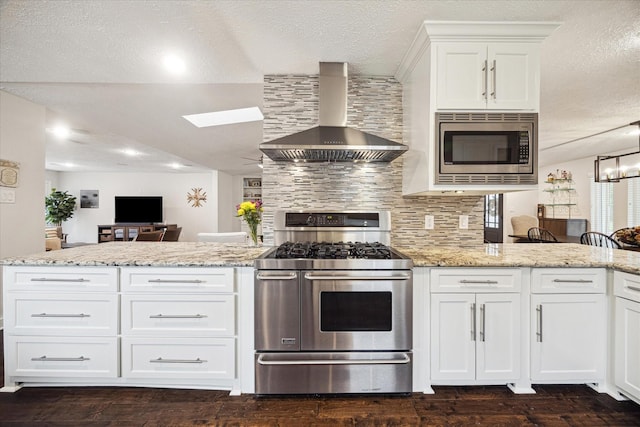 kitchen featuring wall chimney range hood, white cabinets, stainless steel appliances, a peninsula, and a skylight