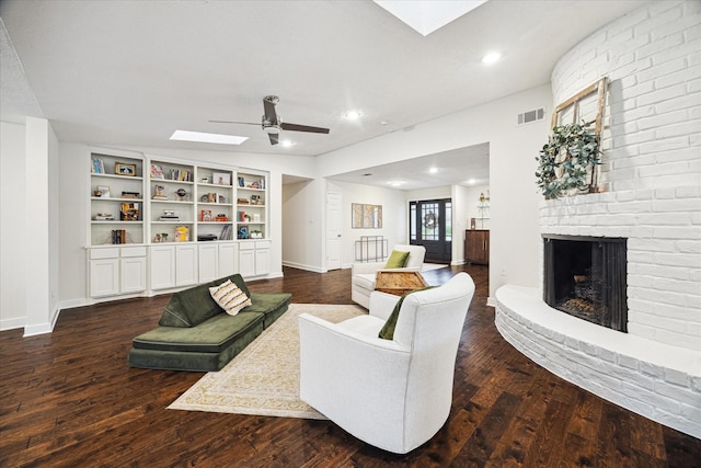 living area with ceiling fan, a brick fireplace, dark wood finished floors, and visible vents