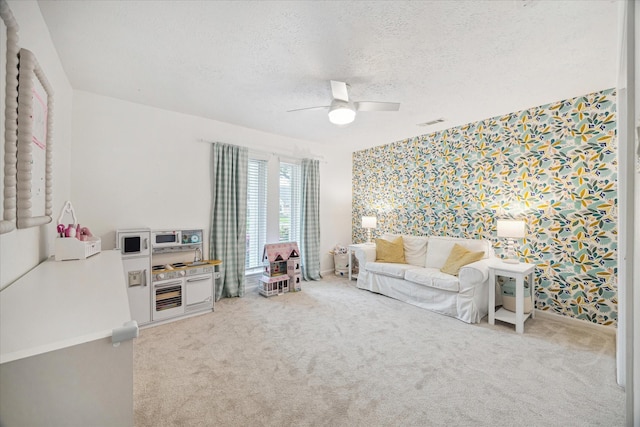 living area featuring visible vents, ceiling fan, wallpapered walls, a textured ceiling, and carpet flooring