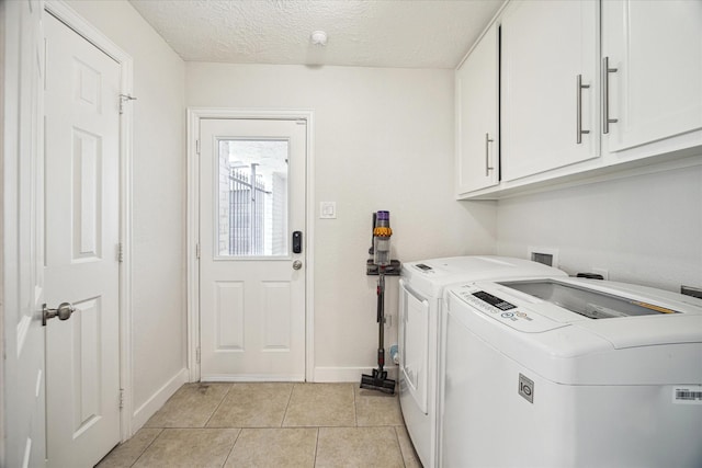 washroom with a textured ceiling, washing machine and clothes dryer, cabinet space, light tile patterned floors, and baseboards