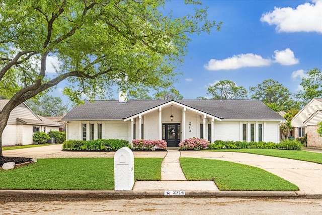 mid-century home featuring a chimney, driveway, brick siding, and a front yard