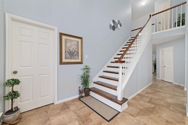 stairs featuring baseboards, stone finish flooring, and a towering ceiling