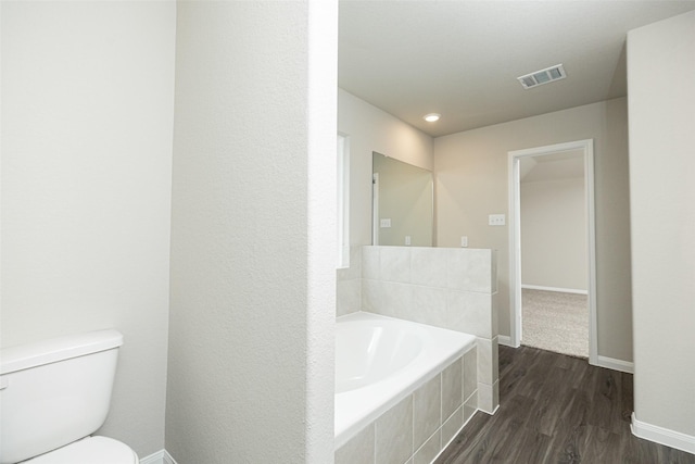 bathroom featuring toilet, baseboards, wood finished floors, visible vents, and a garden tub
