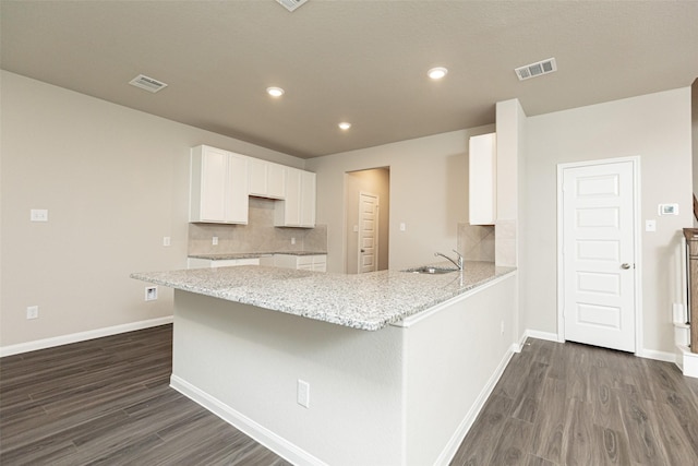 kitchen with visible vents, a sink, light stone counters, a peninsula, and dark wood-style floors