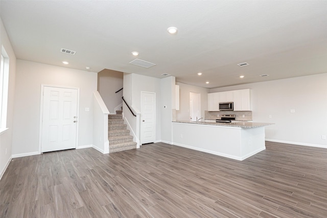 unfurnished living room featuring recessed lighting, baseboards, stairs, and wood finished floors
