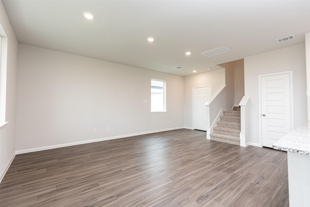 unfurnished living room featuring baseboards, visible vents, wood finished floors, and stairway