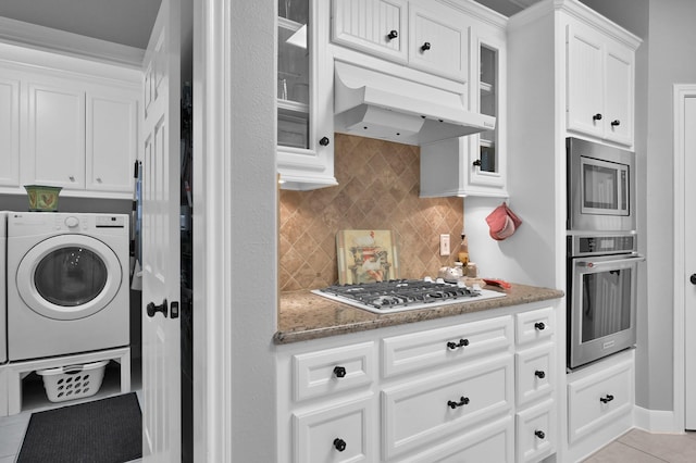 5 Highland Hollow Dr, Conroe, TX 77304 - kitchen with appliances with stainless steel finishes, washer / clothes dryer, under cabinet range hood, white cabinetry, and decorative backsplash