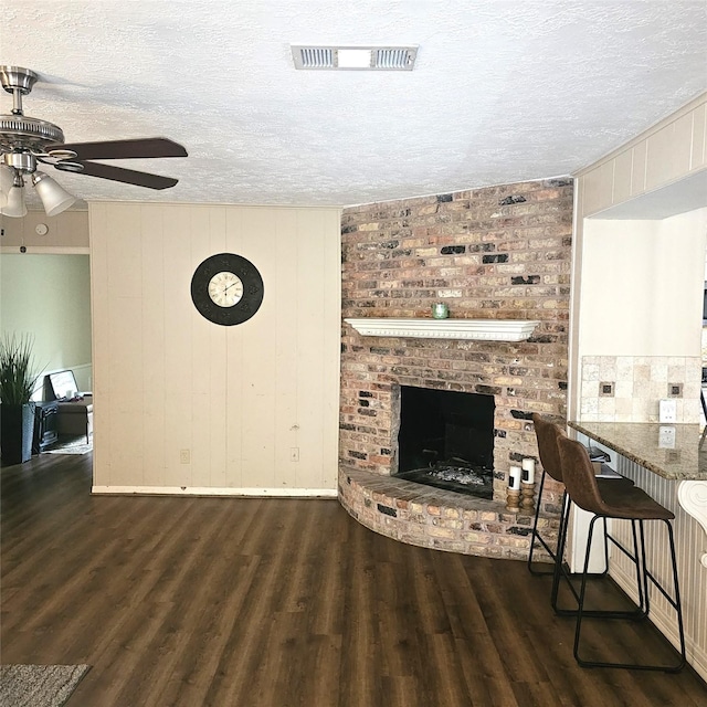 living room with a textured ceiling, ceiling fan, visible vents, and wood finished floors