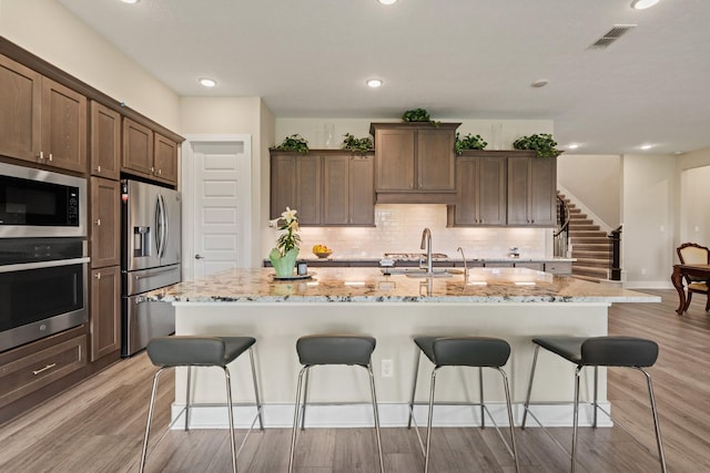 720 Serenity View Ln, Katy, TX 77493 - kitchen with appliances with stainless steel finishes, a sink, a breakfast bar area, an island with sink, and light wood-style flooring