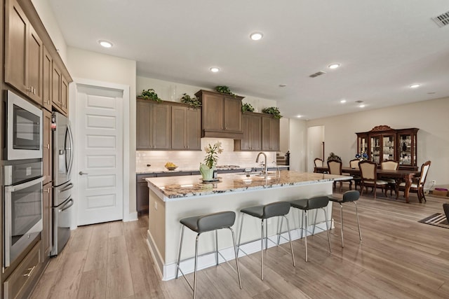 720 Serenity View Ln, Katy, TX 77493 - kitchen with decorative backsplash, a breakfast bar area, light stone countertops, light wood finished floors, and stainless steel appliances