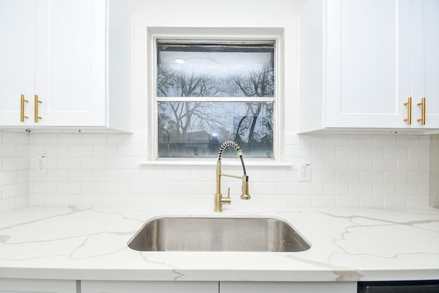details with a sink, decorative backsplash, light stone countertops, and white cabinetry