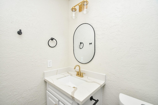 half bathroom featuring vanity, a textured wall, and toilet