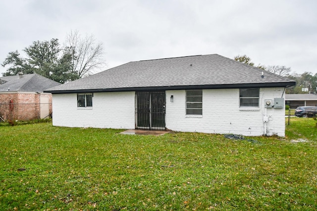 rear view of property featuring roof with shingles, fence, a lawn, and brick siding