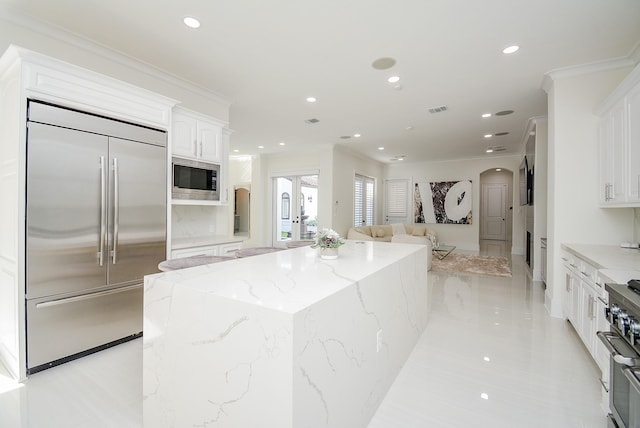 kitchen featuring a kitchen island, arched walkways, white cabinets, built in appliances, and recessed lighting