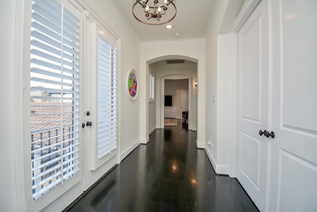 corridor featuring ornamental molding, baseboards, dark wood-style floors, arched walkways, and a notable chandelier