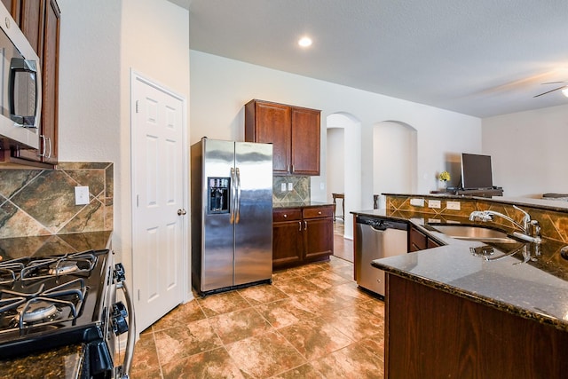 kitchen with dark stone counters, arched walkways, tasteful backsplash, a sink, and stainless steel appliances