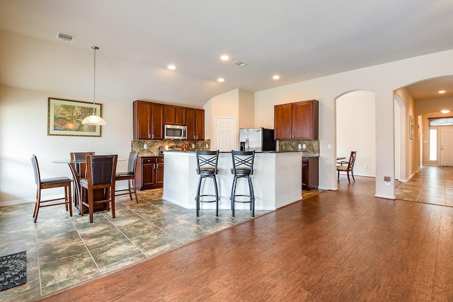 kitchen featuring arched walkways, appliances with stainless steel finishes, decorative backsplash, and visible vents