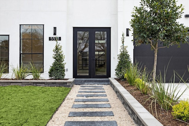 view of exterior entry featuring a lawn, french doors, and stucco siding