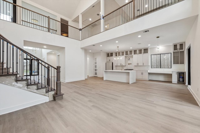 unfurnished living room with visible vents, light wood-type flooring, stairs, and a towering ceiling