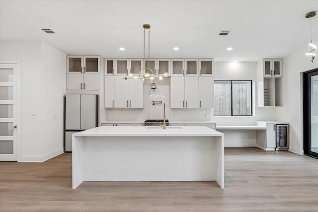 kitchen with visible vents, a center island with sink, fridge, light countertops, and white cabinetry
