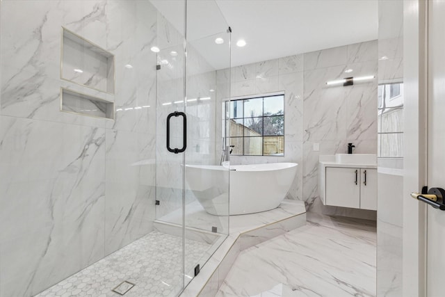 full bathroom featuring a soaking tub, tile walls, a marble finish shower, and vanity