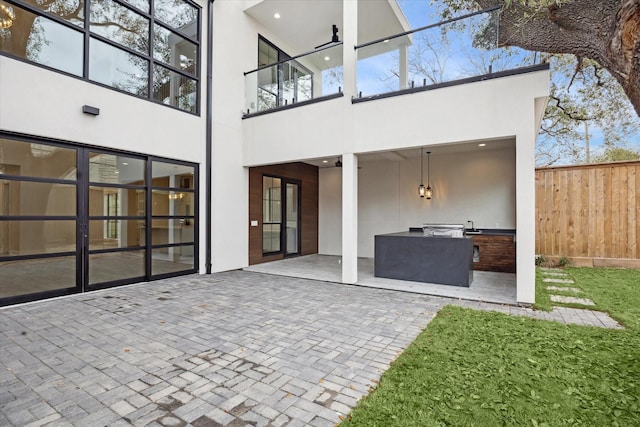 rear view of property featuring fence, exterior kitchen, stucco siding, a patio area, and a balcony