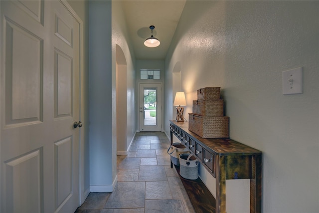 entryway featuring arched walkways, baseboards, and stone tile floors