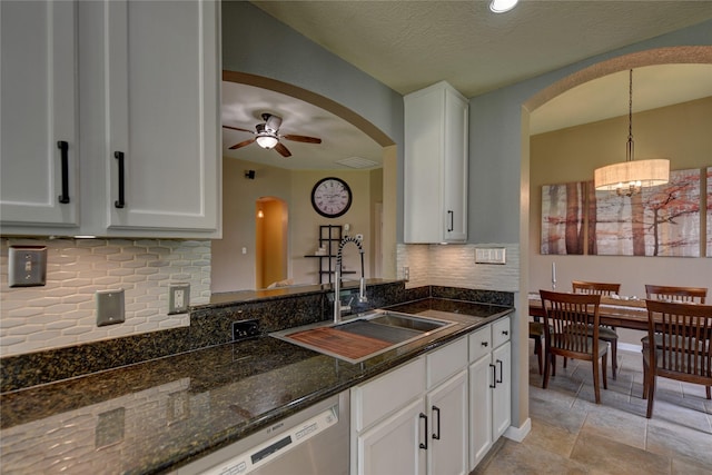 kitchen featuring decorative backsplash, white cabinetry, arched walkways, a sink, and ceiling fan with notable chandelier
