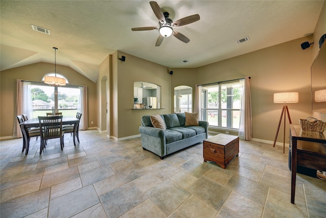 living room featuring visible vents, plenty of natural light, ceiling fan with notable chandelier, and stone tile flooring