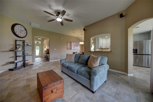 living room featuring visible vents, stone tile floors, baseboards, arched walkways, and a ceiling fan