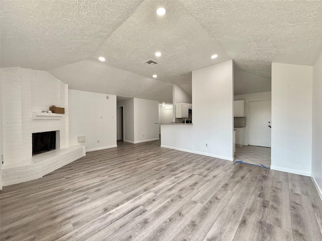 6410 Rancho Blanco Ct, Houston, TX 77083 - unfurnished living room featuring vaulted ceiling, a textured ceiling, light wood finished floors, a brick fireplace, and baseboards