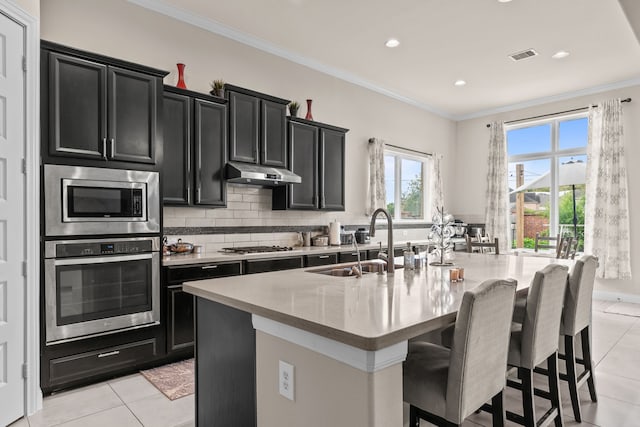 3422 Leaning Willow Dr, Katy, TX 77494 - kitchen with appliances with stainless steel finishes, a sink, dark cabinetry, under cabinet range hood, and an island with sink