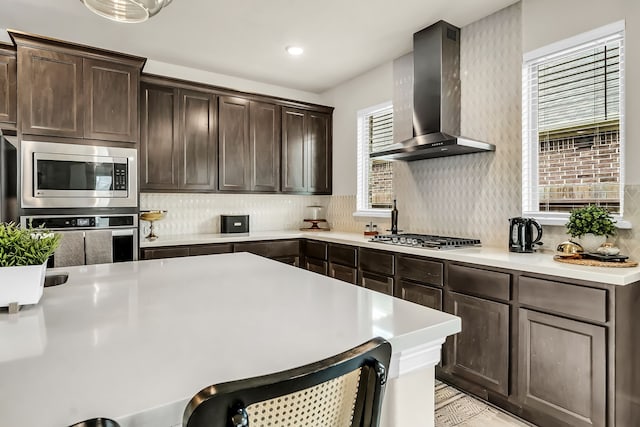 32927 Franklin Brooks Dr, Brookshire, TX 77423 - kitchen featuring wall chimney range hood, dark brown cabinets, appliances with stainless steel finishes, light countertops, and decorative backsplash