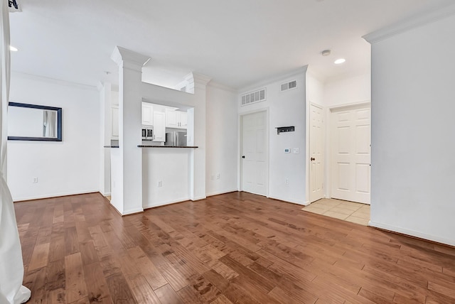 unfurnished living room featuring baseboards, ornamental molding, wood finished floors, and visible vents