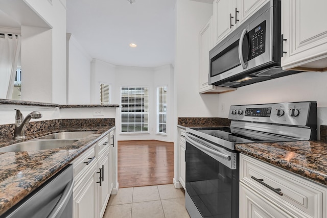 kitchen featuring white cabinets, stainless steel appliances, a sink, and dark stone countertops