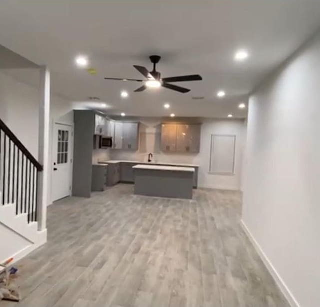 kitchen with stainless steel microwave, baseboards, ceiling fan, a kitchen island, and light countertops