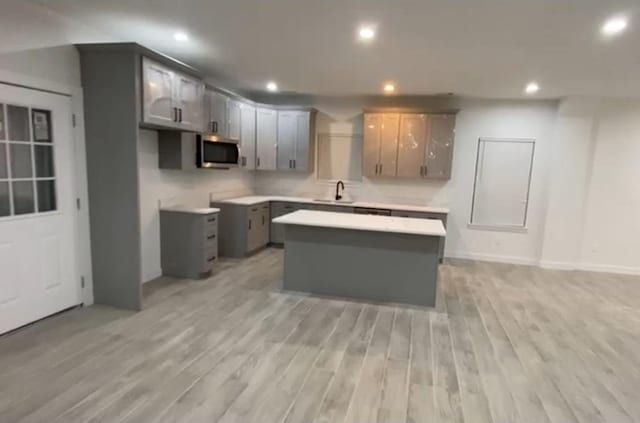 kitchen featuring stainless steel microwave, light wood-style flooring, a center island, recessed lighting, and a sink