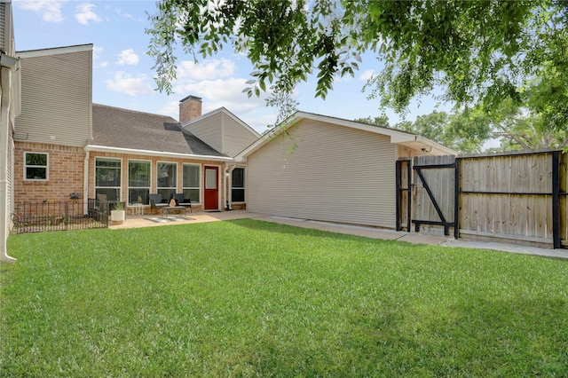 back of house featuring a chimney, a gate, brick siding, a yard, and a patio