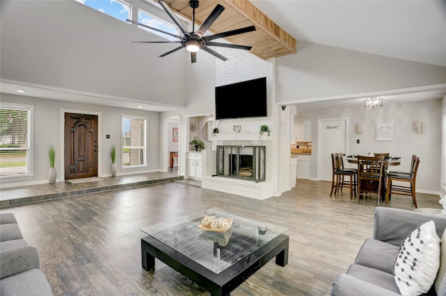 living area with a fireplace, light wood-type flooring, high vaulted ceiling, baseboards, and ceiling fan with notable chandelier