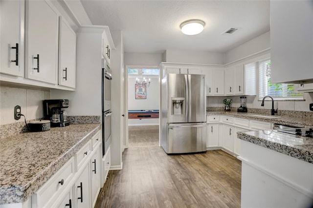 kitchen featuring light stone countertops, stainless steel fridge, a sink, white cabinetry, and wood finished floors