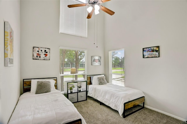 carpeted bedroom featuring a ceiling fan, a high ceiling, and baseboards