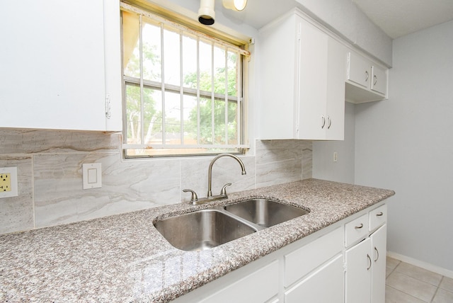 kitchen with light tile patterned floors, a sink, white cabinets, decorative backsplash, and light stone counters