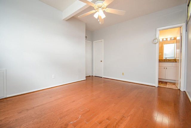 unfurnished bedroom with baseboards, beamed ceiling, light wood finished floors, and connected bathroom