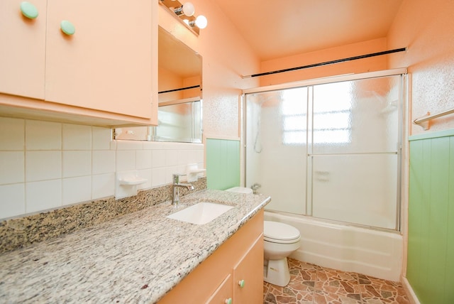 full bathroom with wainscoting, vanity, toilet, and bath / shower combo with glass door